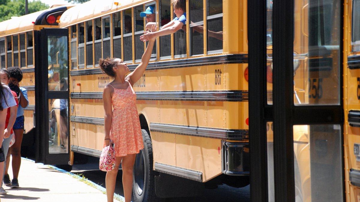 Girl stands next to bus and high fives with someone inside the bus